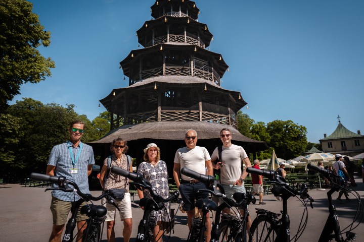 Five people with bicycles in front of a pagoda-style building on a sunny day.