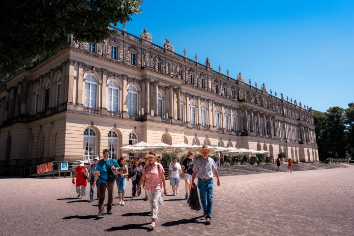 Group of tourists walks past a grand historic building under a clear blue sky.
