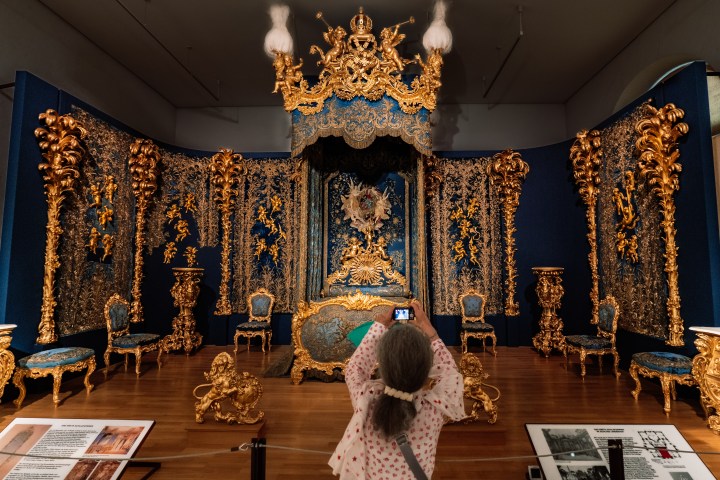 Person photographing an ornate, gold and blue baroque-style room exhibit in a museum.
