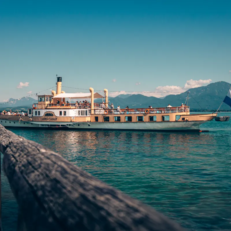 Vintage boat on a lake with mountains and blue sky in the background.