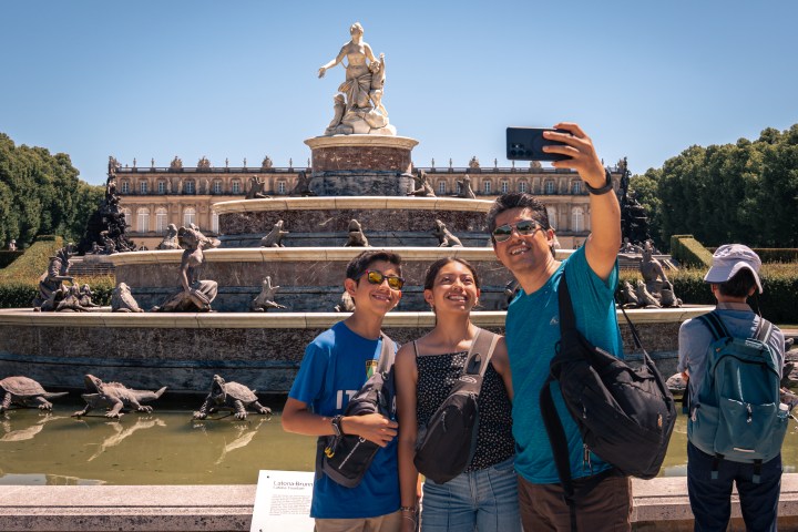 Family taking selfie in front of a large fountain statue on a sunny day.