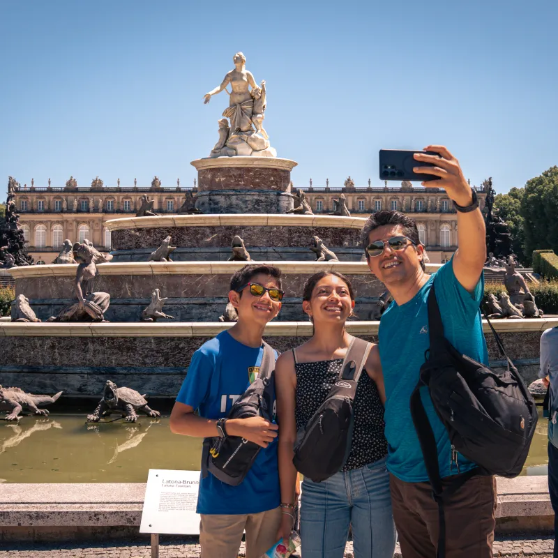 Family taking selfie in front of a large fountain statue on a sunny day.