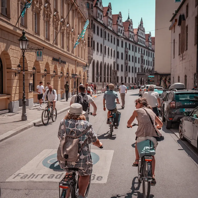 Cyclists riding on a city street lined with historic buildings and parked cars.