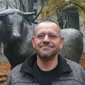 Man standing in front of a bull statue with autumn trees in the background.