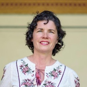 Woman with curly hair smiling, wearing a floral embroidered blouse.
