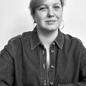 Black and white portrait of a person with short hair, wearing a denim shirt and hoop earrings.