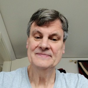 Man with short hair smiling, wearing a gray shirt indoors.