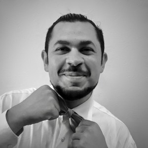 Man smiling while adjusting a tie against a plain background.