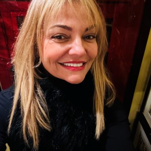 Smiling woman with blonde hair and black scarf in a red setting.