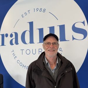 Man smiling in front of a sign reading 'Radius Tour Est 1988'.