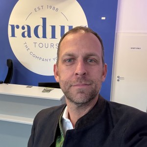 Man taking a selfie in front of a Radius Tours sign at a reception area.