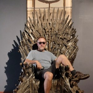 Person wearing sunglasses sits on an iron throne replica.