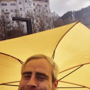 Person smiling under a yellow umbrella with a castle in the background.