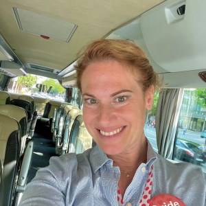 Woman with 'Guide' badge smiling inside a bus with empty seats.