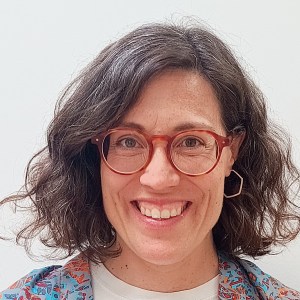 Woman with shoulder-length curly hair, wearing glasses, smiling.