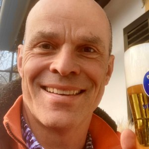 Man smiling and holding a glass of beer outdoors.