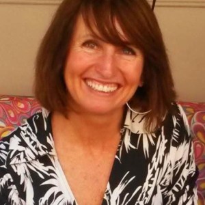 Smiling woman with glasses on head, wearing a black and white patterned shirt.