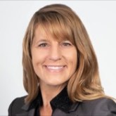 Smiling woman with brown hair in a blazer on a light background.