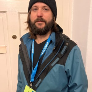 Person in a beanie and jacket with a blue lanyard standing indoors.