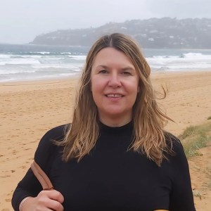 Person with long hair on a beach with waves and hills in the background.