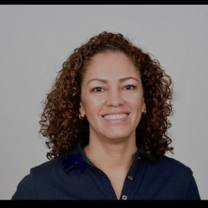 Smiling person with curly hair wearing a navy shirt against a neutral background.