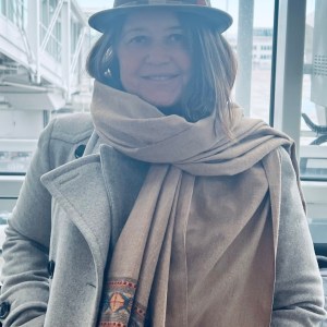 Person in a gray coat and hat at an airport terminal.
