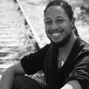 Black and white image of a smiling person sitting by railway tracks.